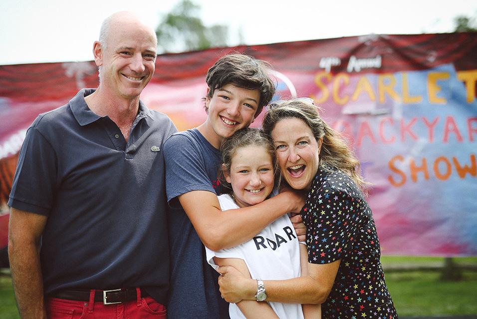 A family with a mom, dad, son, and daughter smiles at the camera while hugging. 